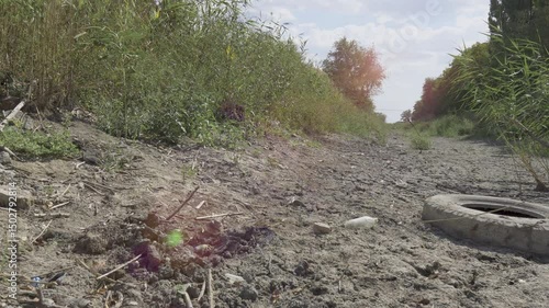 Dry, cracked soil is overgrown with sparse grass. Drought and global warming affect the riverbed in summer. Concept of drought, global warming and water shortage. Camera moves from left to right