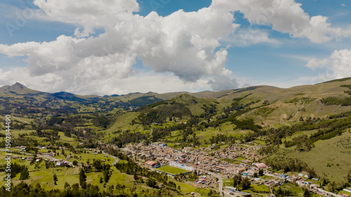 Drone aerial view of an Andean village in Cusco, Peru, surrounded by green mountains and partly cloudy sky