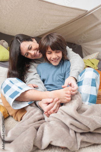 Mother hugging son from behind while tickling his feet with a smile