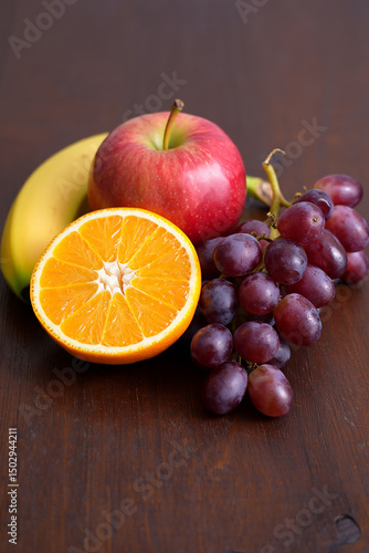 Fresh and colorful still life arrangement of apple, banana, orange, and grapes on a wooden table, showcasing healthy eating and natural sweetness