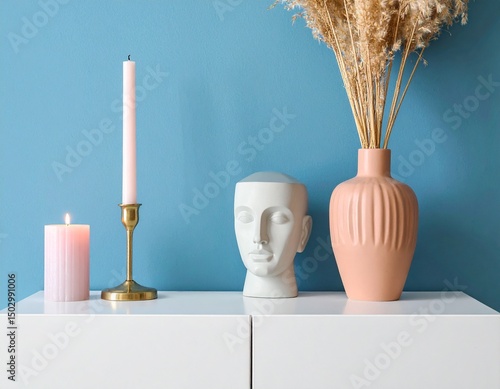 Modern console table with pastel candle, abstract head sculpture, and terracotta vase agains