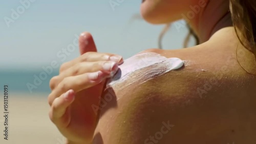 A woman applying sunscreen on her shoulder at the beach.