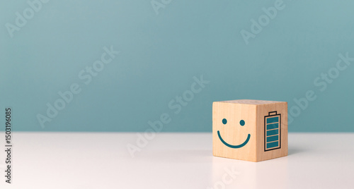 Work motivation, mental health assessment, battery, energy, employee happiness and positive attitude. Wooden block with smile face emoticon with full level energy battery in the office