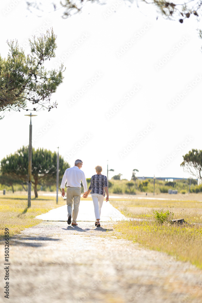 Fototapeta premium Senior couple walking away on path holding hands in park
