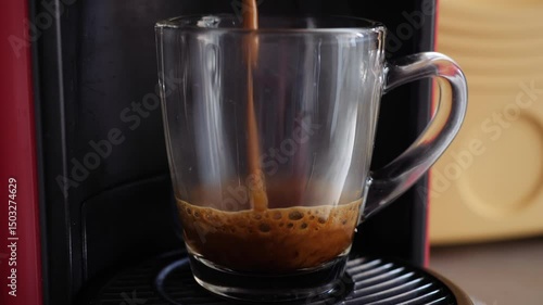 Espresso extraction from pod coffee maker into transparent mug.
Video of hot coffee being brewed from a capsule machine, cascading in a smooth, rich brown stream into a transparent glass mug.
