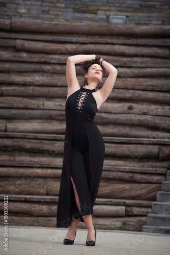 woman in black jumpsuit posing confidently in front of wooden wall