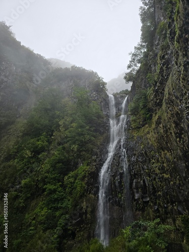 Tall waterfall cascading through misty cliffs on Madeira’s Levada das 25 Fontes trail. Rain-soaked rocks and lush vegetation create a wild, serene atmosphere.