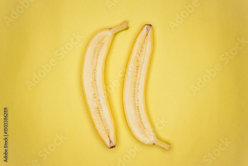Top view photo of one cut in half raw banana on the yellow background