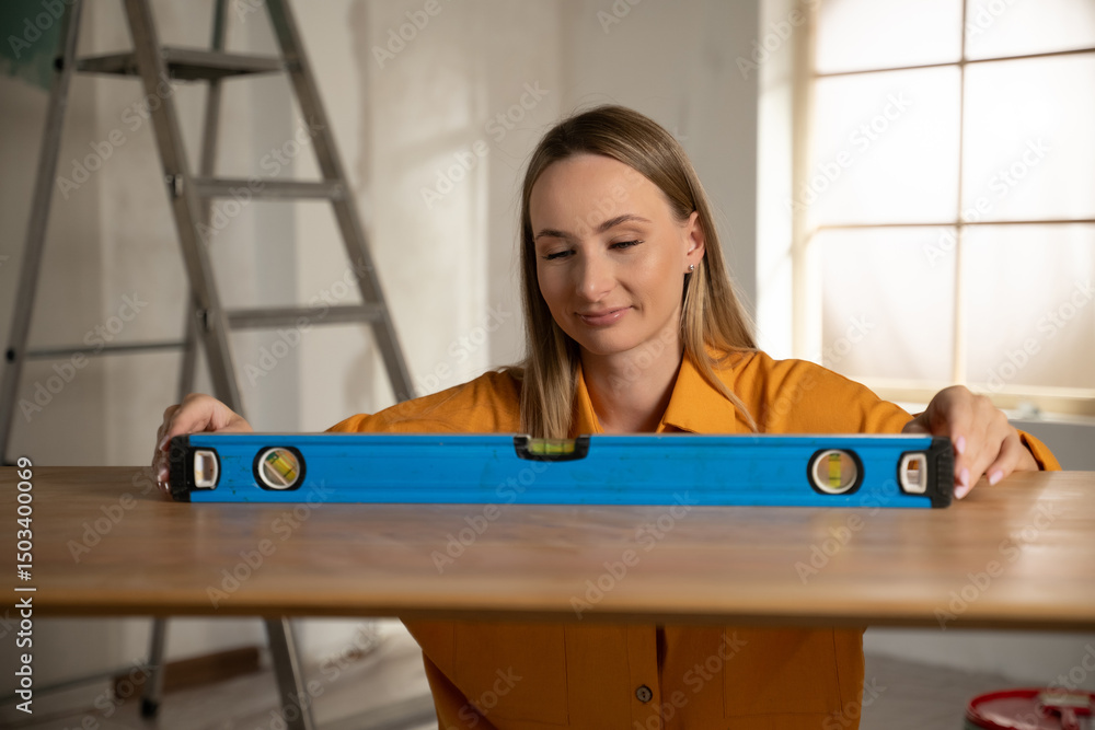 Obraz premium Female worker using a spirit level while installing furniture in a new apartment, carefully checking the alignment of a wooden board to ensure it is perfectly straight and balanced