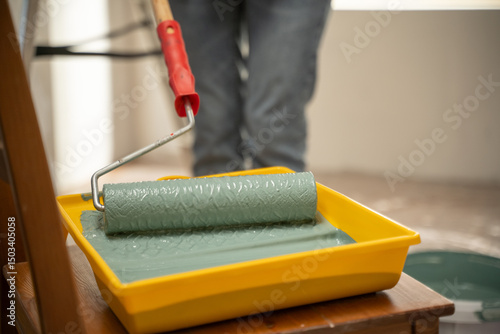 Painter dipping a patterned paint roller into a tray filled with vibrant green paint, getting ready to transform a wall during an exciting home renovation project