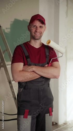 Professional house painter smiling with arms crossed, holding a paint roller in a freshly painted room, showcasing confidence and expertise in home renovation