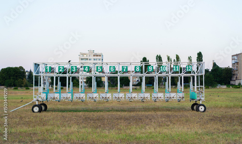 Starting gate positioned on a grassy field near residential buildings during the early evening hours