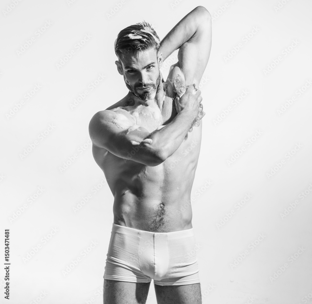 Fototapeta premium Handsome guy in boxer shorts washing body with moisturizing shower gel. Morning routine, self hygiene, skincare and spa. Muscular man taking shower and washing body with soap foam. Black and white.