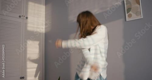 Cheerful girl in casual clothes dancing and moving energetically while listening to cheerful and upbeat rock music at home