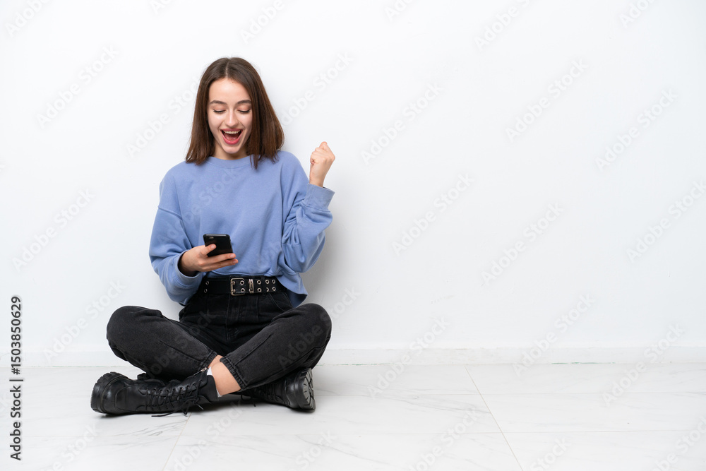 Young Ukrainian woman sitting on the floor isolated on white background surprised and sending a message Young Ukrainian woman sitting on the floor isolated on white background surprised and sending a message