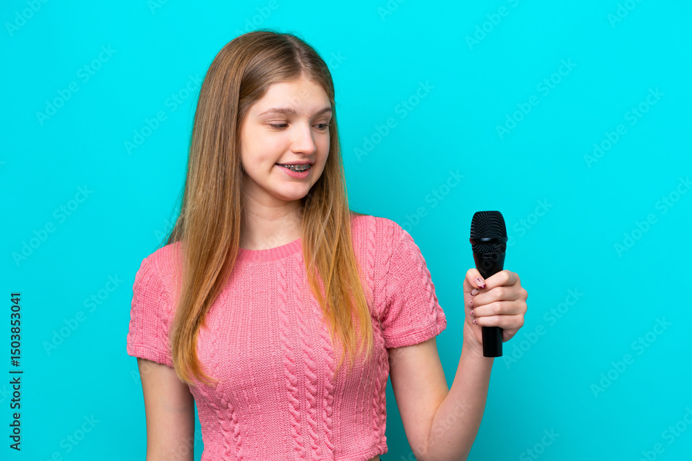 Singer Russian girl picking up a microphone isolated on blue background with happy expression Singer Russian girl picking up a microphone isolated on blue background with happy expression