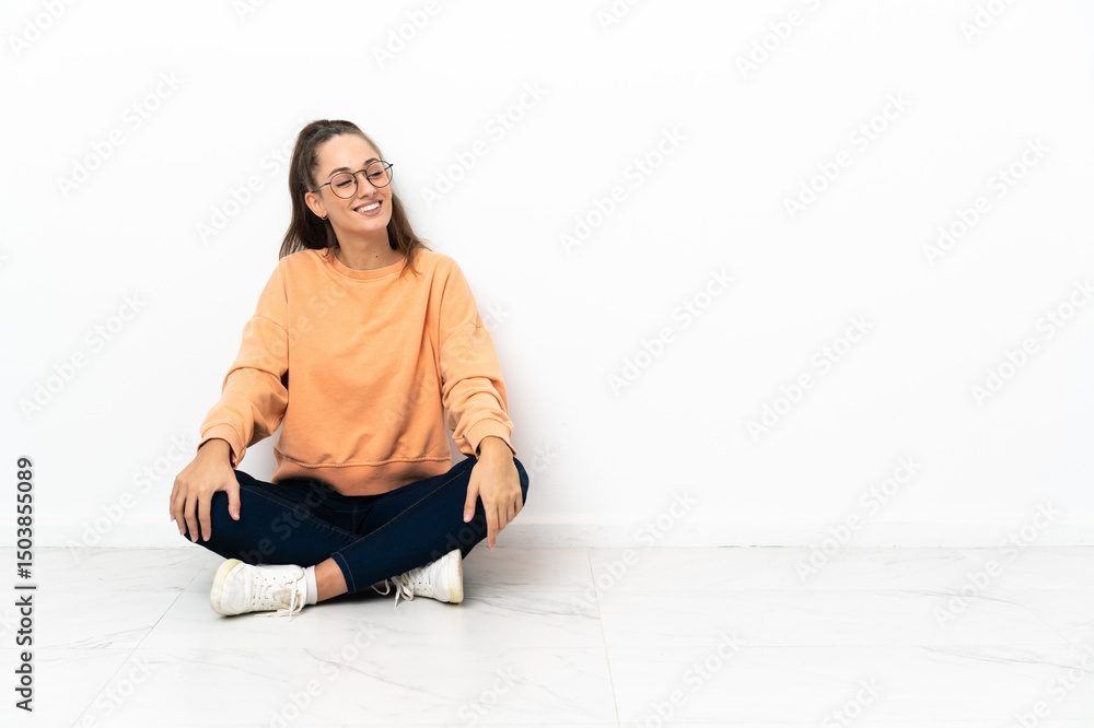 Fototapeta premium Young woman sitting on the floor looking to the side and smiling