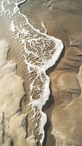 Aerial view shows white foamy waves washing across tan sand forming natural texture