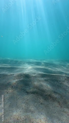 Underwater view of a shallow shoreline with beautiful light flickering over textured sand in aqua coloured clear water. Captured in slow motion from below the ocean's surface.