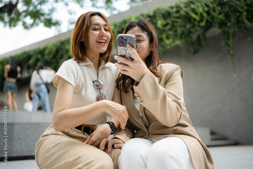 Fototapeta premium Happy asian colleagues browsing social media content during working day in outdoor office building using 5g wireless