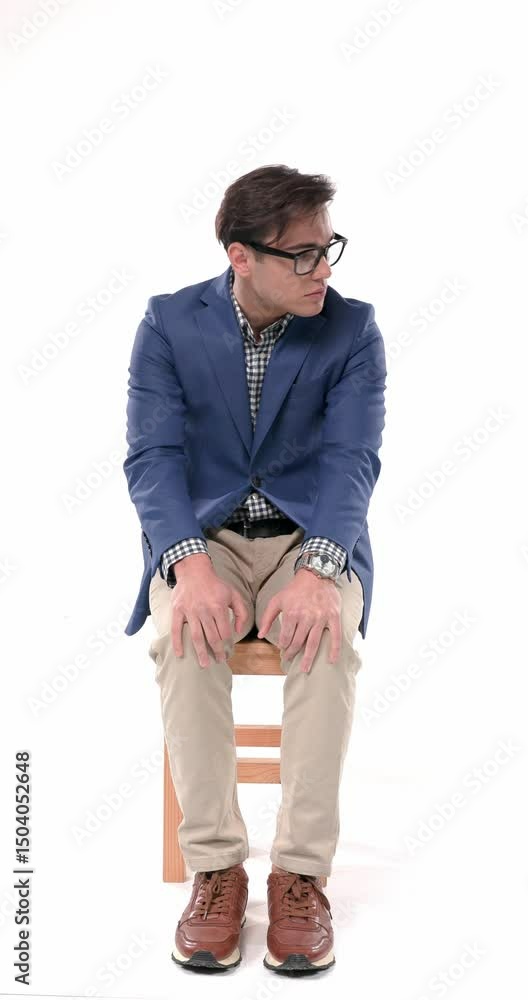 project video of timid young man with glasses holding palms on knees, looking both sides and being anxious while sitting on white background project video of timid young man with glasses holding palms on knees, looking both sides and being anxious while sitting on white background