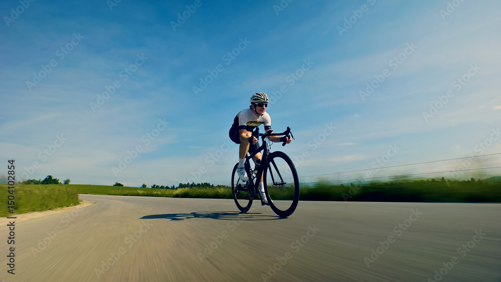 Obraz premium A thrilling close-up shot of a helmeted cyclist skillfully navigating a winding road, surrounded by lush greenery and a clear blue sky. The dynamic perspective emphasizes the speed and intensity of.