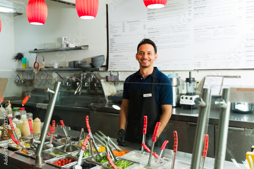 Bild auf Leinwand Smiling restaurant employee working at salad bar with fresh ingredients