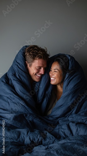 A couple is lying on the bed, wrapped in an extremely large and soft navy blue down comforter that covers them from head to toe
