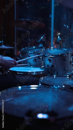 Close-up of a drum set illuminated by dramatic blue stage lighting during a live concert performance.