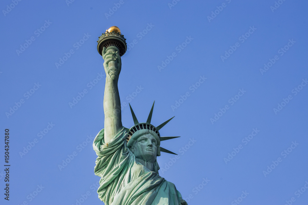 Fototapeta premium Statue of Liberty in New York City on a clear day. Iconic American symbol captured with bright sky and strong lighting.