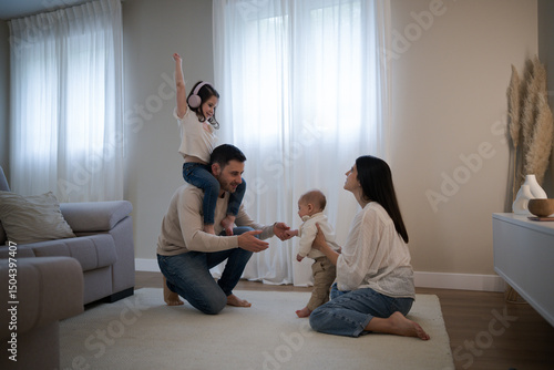 Happy family playing with baby taking first steps at home