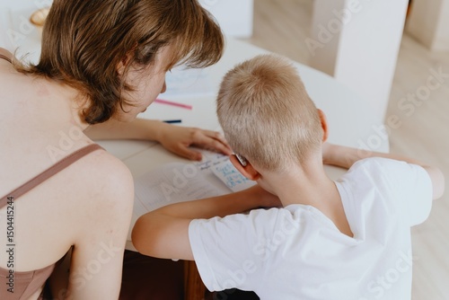 A loving mother and her son work together on homework at the kitchen table, symbolizing family support, education, and care. The scene highlights the importance of parental guidance