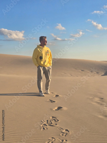 Canvas Print A young man strolls through the tranquil sand dunes of Denmark, leaving a trail of footprints in the soft sand