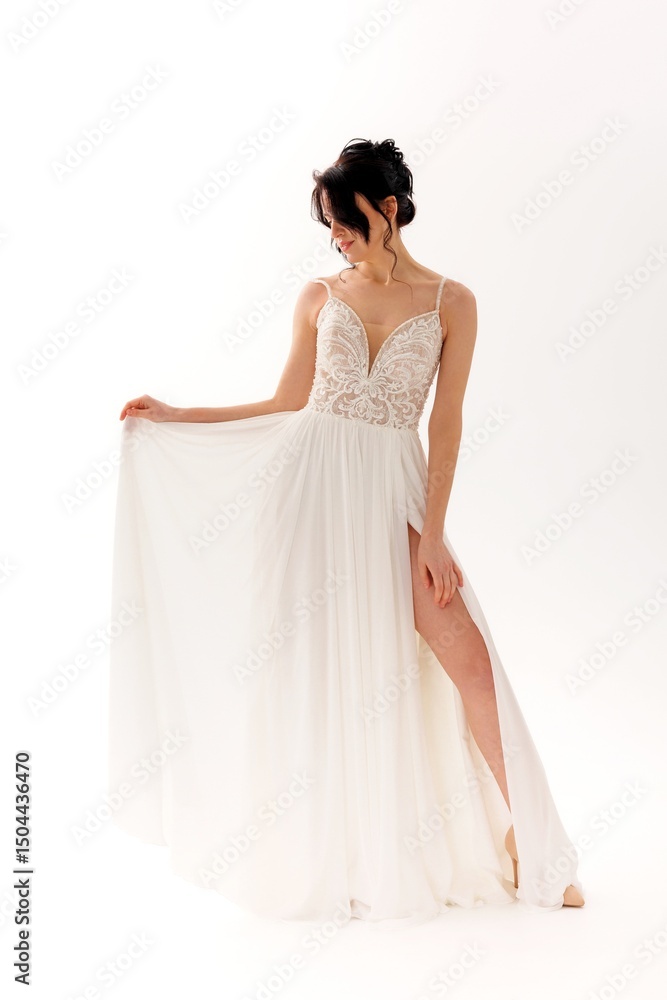 Fototapeta premium Elegant model showcases a flowing white dress with delicate detail in a minimalist studio setting
