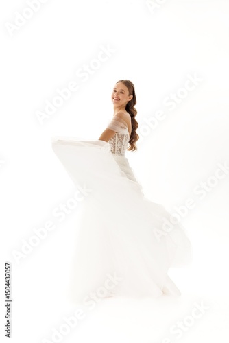 Bride twirls gracefully in elegant wedding gown on a bright white background during a photoshoot at sunset