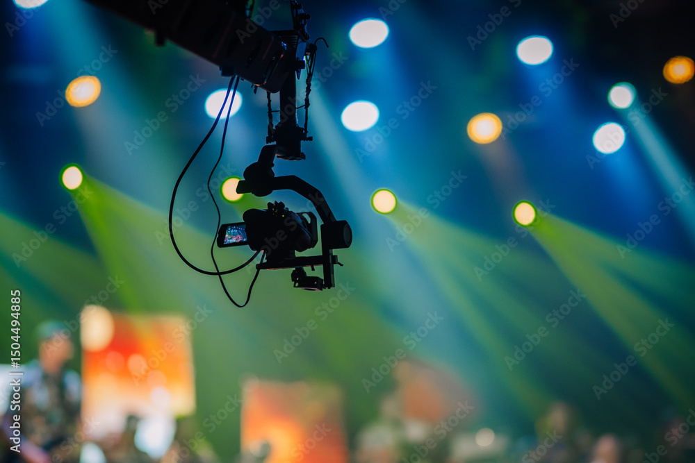Silhouette of a suspended camera filming a live event with vibrant stage lights and colorful blurred background during a concert or performance.. Silhouette of a suspended camera filming a live event with vibrant stage lights and colorful blurred background during a concert or performance..