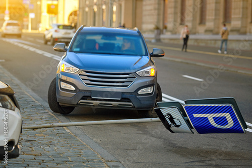 Accident in parking lot with knocked down pole bearing parking sign and location plate, suv in background with hazard lights on after careless driving. Fallen pole, result of collision with SUV