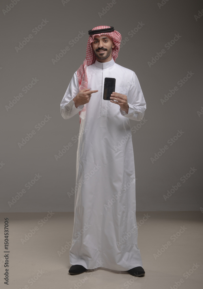 Saudi Arabian man wearing traditional thobe and shemagh using a smartphone, making a call and smiling. Concept of communication, technology, and modern lifestyle in the Gulf region Saudi Arabian man wearing traditional thobe and shemagh using a smartphone, making a call and smiling. Concept of communication, technology, and modern lifestyle in the Gulf region