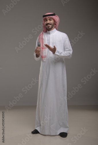 Saudi man in traditional attire using a car remote and pointing with a smile. Concept of car security, remote access, smart vehicle technology, and modern lifestyle in Saudi Arabia.