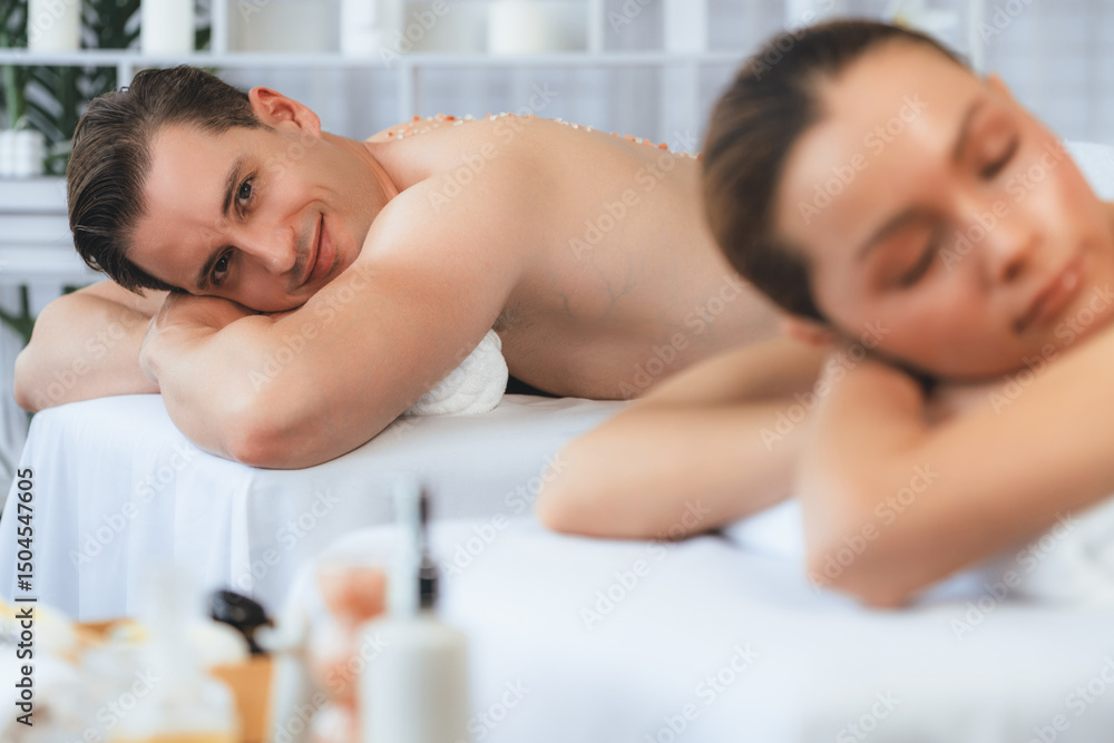 Obraz premium Blissful couple customer having exfoliation treatment in luxury spa salon with warmth candle light ambient. Salt scrub beauty treatment in health spa body scrub. Quiescent