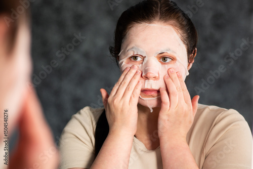 Wallpaper Mural Close up of female adjusting sheet mask on face in modern bathroom. Ideal for cosmetic ads or spa treatment visuals. Torontodigital.ca