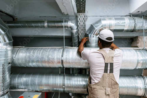 Quadro su tela Skilled worker installing metal ductwork in a commercial building during a maint