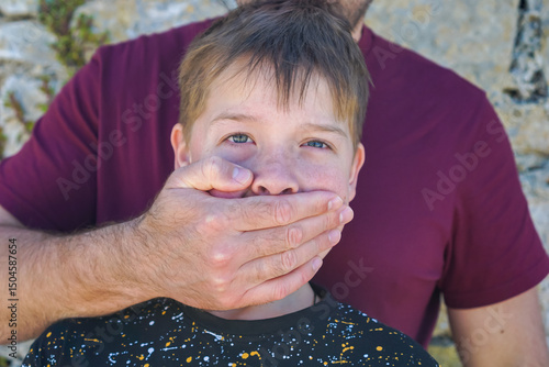 Fotografie Adult hand covering young boys mouth, boy gazing at camera with distressed expre