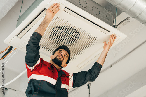 Tableau sur toile Technician installs ceiling air conditioning unit in modern office space during