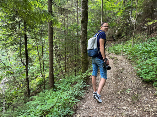 A man carrying a backpack is happily walking down a scenic path in the woods