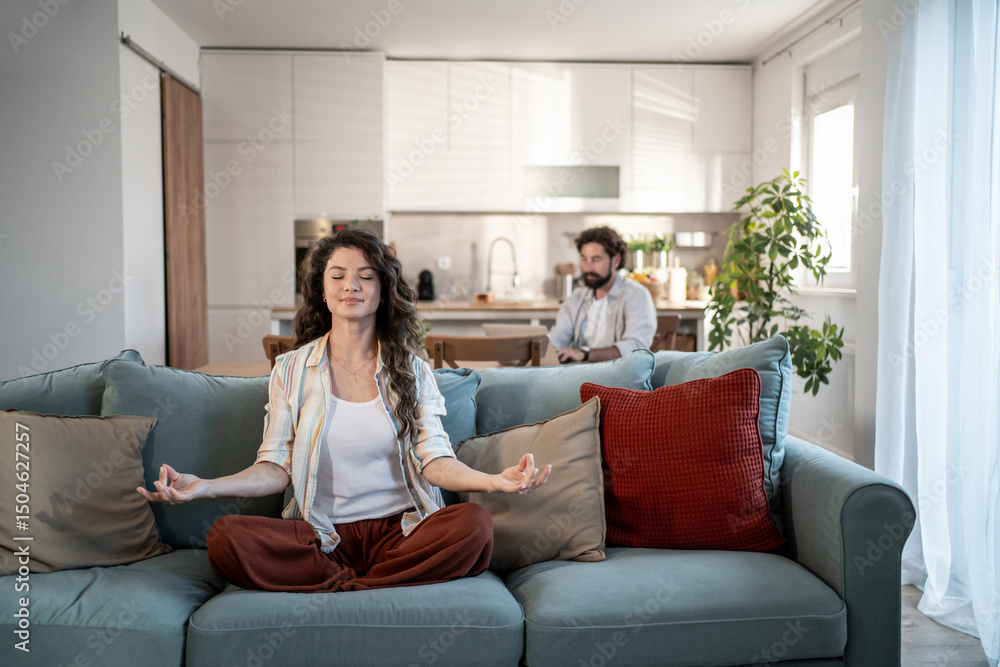Woman meditating on sofa while man working from home Woman meditating on sofa while man working from home