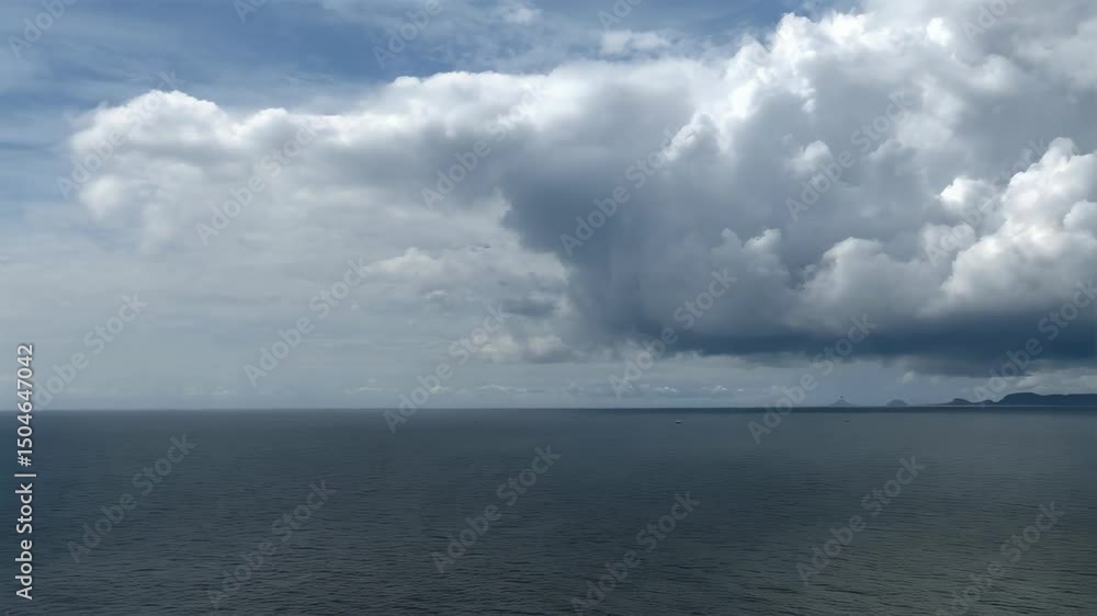 Moody seascape featuring dramatic storm clouds over a calm ocean with distant islands and a rocky headland. Moody seascape featuring dramatic storm clouds over a calm ocean with distant islands and a rocky headland.