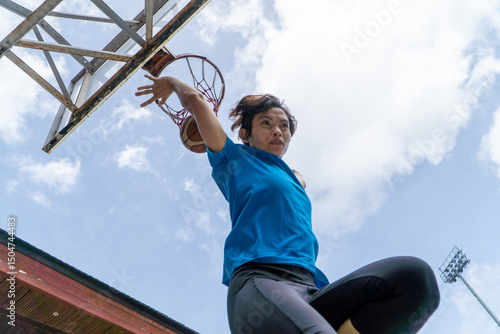 Denpasar, 13 Feb 23: A young athlete performs a slam dunk at a street basketball court under the midday sun in Bali, Indonesia.