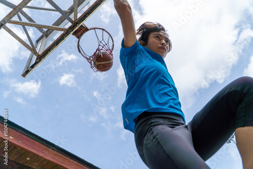 Denpasar, 13 Feb 23: A young athlete performs a slam dunk at a street basketball court under the midday sun in Bali, Indonesia.