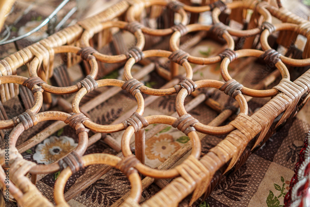 Obraz premium Close-up shot of an interwoven, round-patterned wicker furniture piece, displaying craftsmanship with intricate detailing, paired against a patterned fabric backdrop, ideal for home decor.
